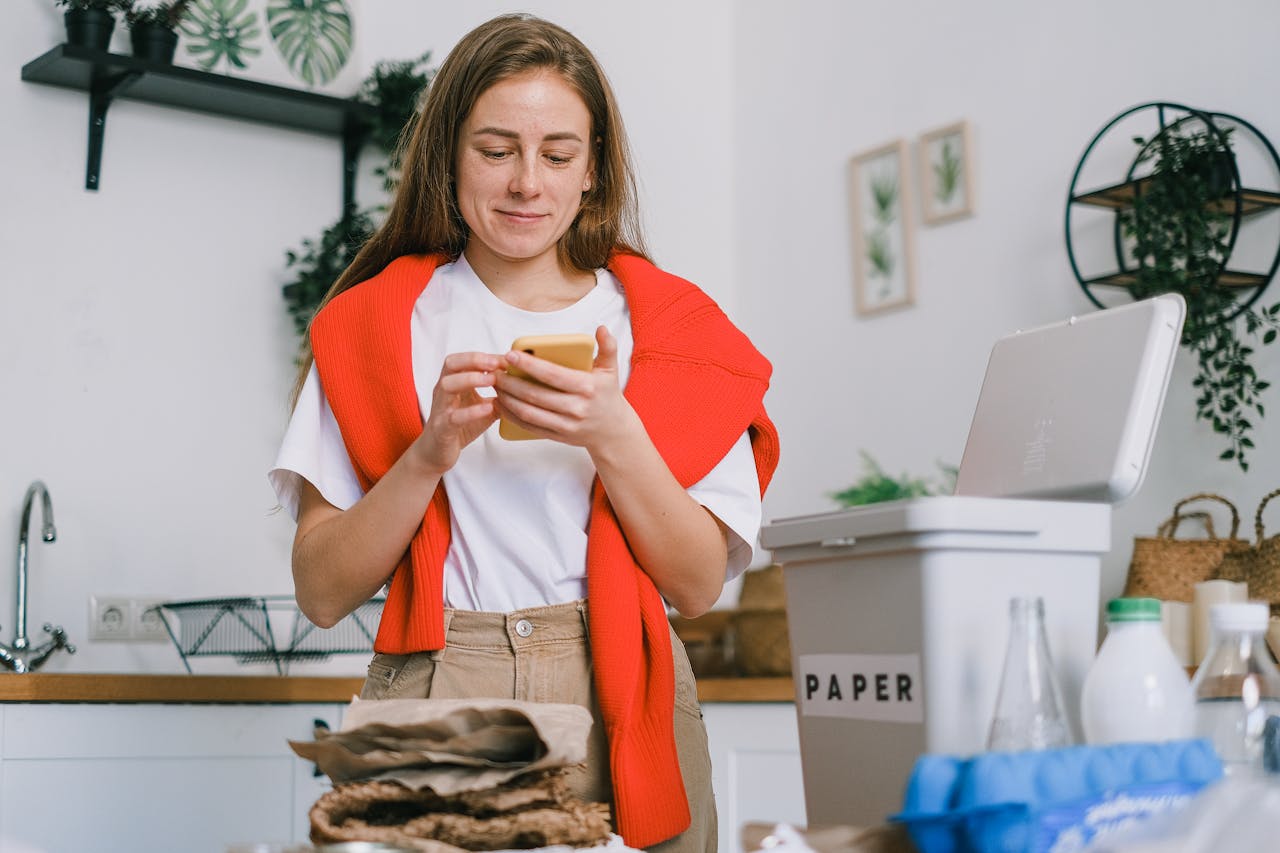 who-we-are Cheerful female browsing mobile phone and standing at table with sorted paper and plastic waste